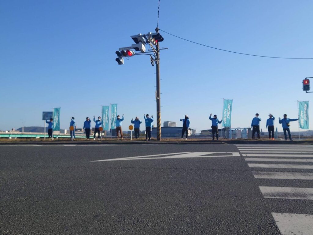 交差点での反対側でチームのメンバーが道路に向かって手を振っている様子